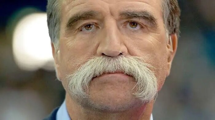 En man med stora gråa mustascher och ett allvarligt ansiktsuttryck.