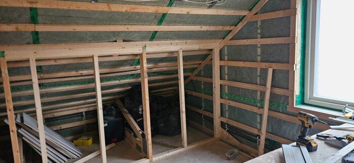 Träram för väggkonstruktion under pågående renovering av ett vindsvåning, med isolering synlig och verktyg på en arbetsbänk.