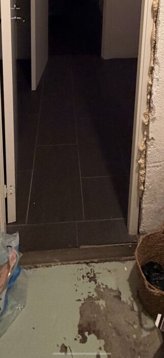 Tröskel mellan två rum med olika golvnivåer, där det ena rummet har klinkergolv och det andra har skadad yta.