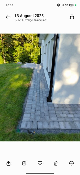 Marksten lagd längs en husvägg, omgiven av gräs. Strålningskyddet breddad till cirka en meter för att förhindra växtlighet och underlätta gång.