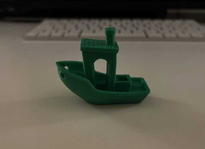 Grön 3D-utskriven prydnadsbåt på ett bord framför ett tangentbord.