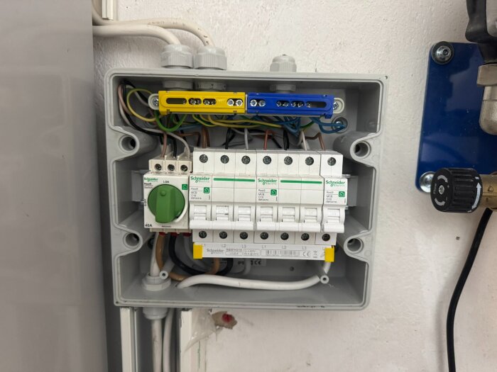 Elektrisk kopplingslåda med automatsäkringar och kablar installerad på en vit vägg.