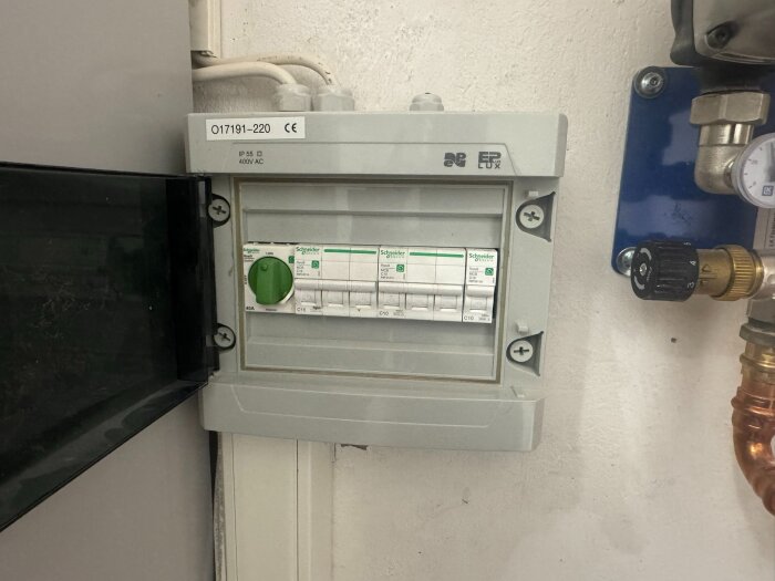Elcentral med snabbsäkringar installerad på vit vägg, omgiven av rör och en mätare.