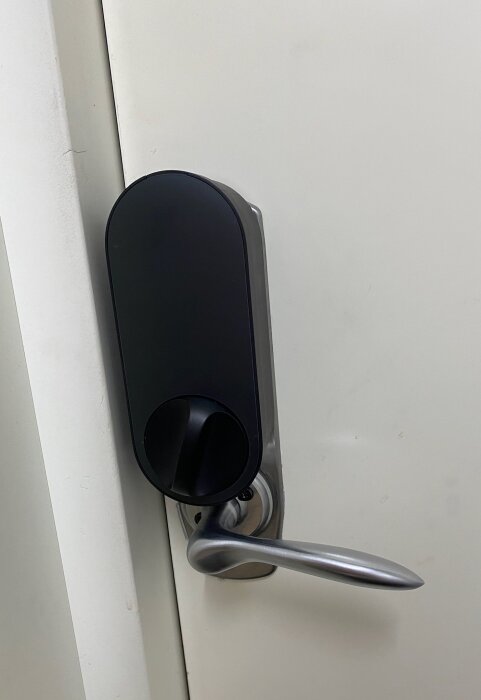 Svart dörrlås ASSA 2002 monterat upp och ner på vit dörr, med silverfärgat dörrhandtag under låsvredet.