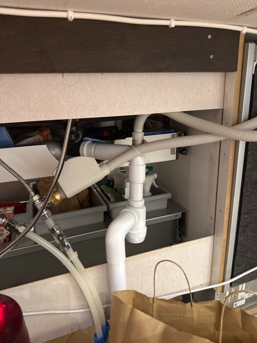 Rörsystem under diskbänk med olika kopplingar och slangar, troligen för en AAV-installation.