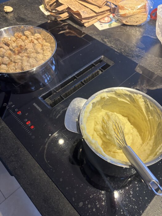 Kastrull med potatismos och stekpanna med köttbullar på en spis.