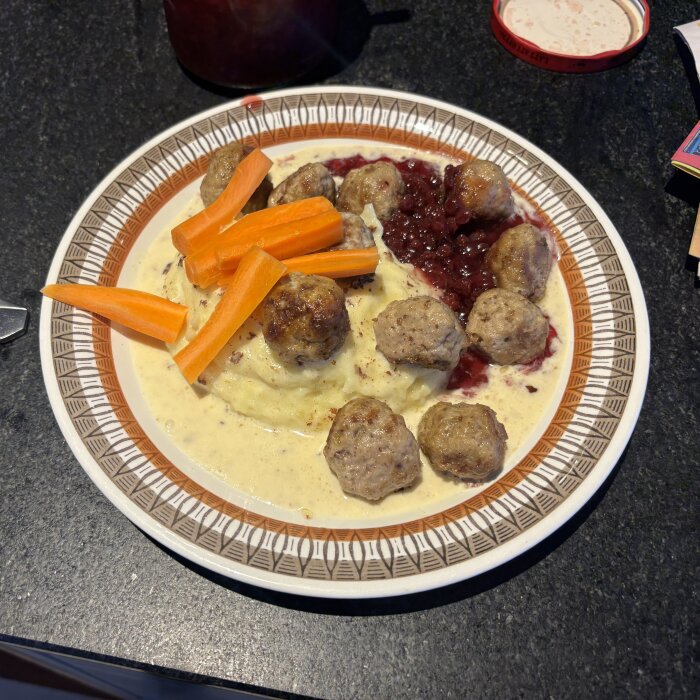 Köttbullar och potatismos på tallrik med lingonsylt och morotsstavar, serverade med gräddsås.