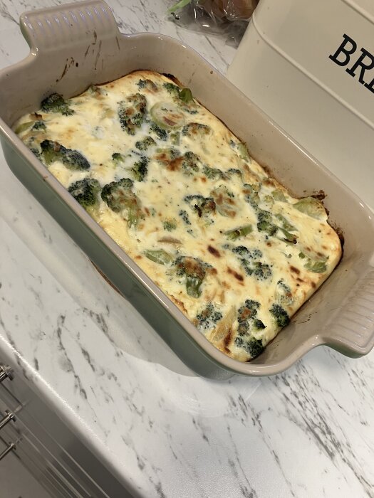 Ugnsform med broccoligratäng på marmorbänk i köket.
