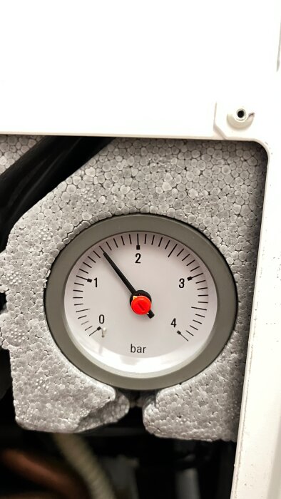Manometer på värmepanna visar tryck på 1,5 bar, omgiven av grå isolering.