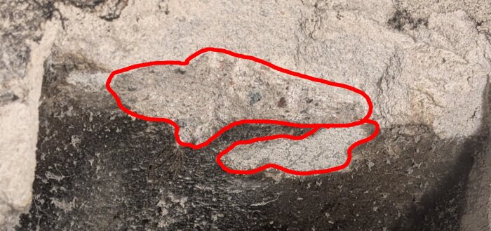 Närbild av en vägg där material har tagits bort, markerat med röd färg. Gruvigt ytskick antyder betong, osäkerhet om asbestinnehåll.