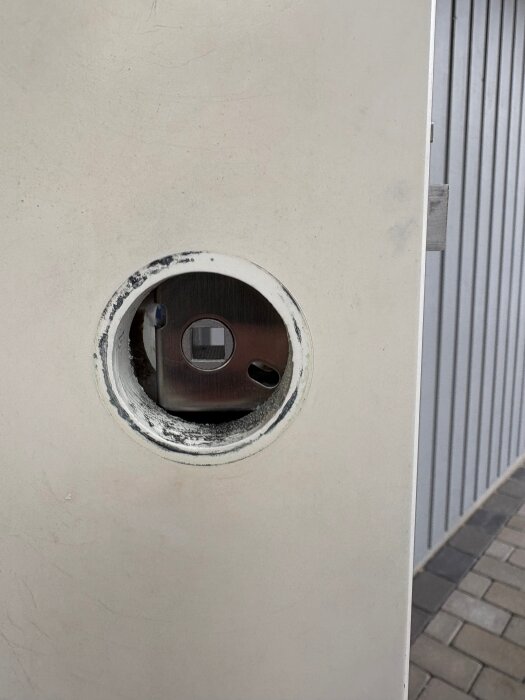 Detalj av ett dörrhandtagshål med en delvis monterad låsenhet i en vit dörr, visar insidan inför installation av ett elektroniskt lås.