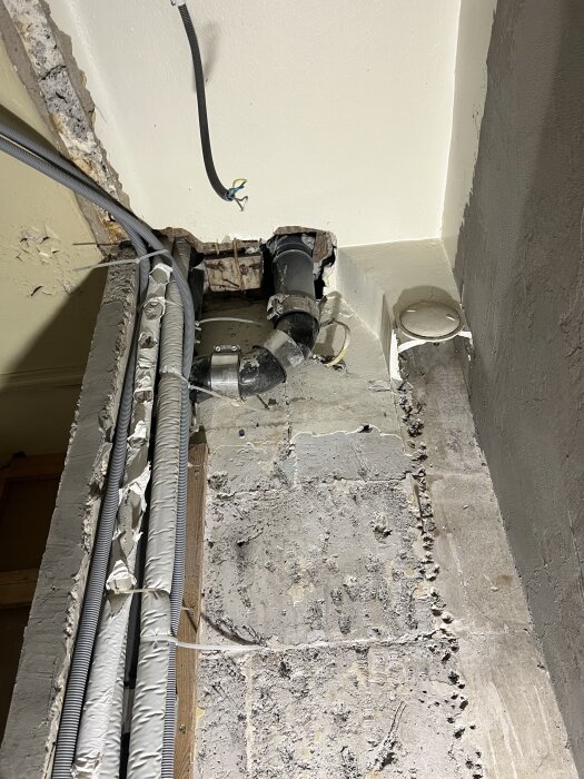 Avslöjade avloppsstam och igenmurad ventilation i ett renoverat badrumstak med synliga rör och kablar.