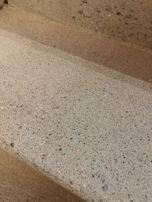 Närbild av en slipad och ren betongtrappa efter borttagning av heltäckningsmatta och lim, visar den råa betongytans struktur och färg.