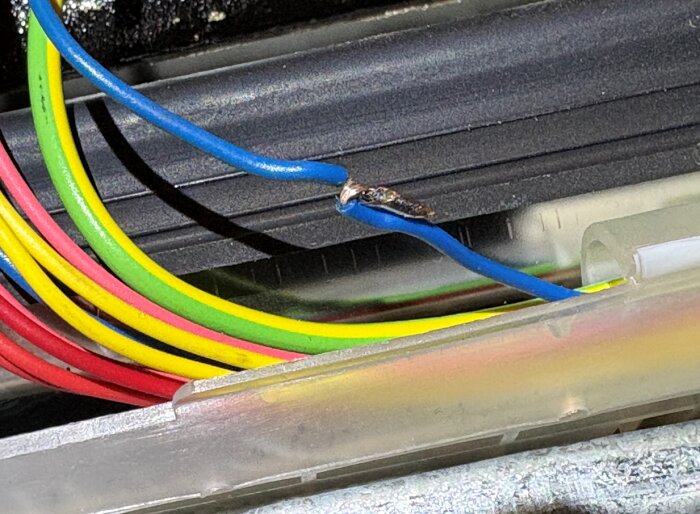 Närbild på en blå kabel med en skarv, omgiven av andra färgade kablar, från en diskmaskin under felsökning.