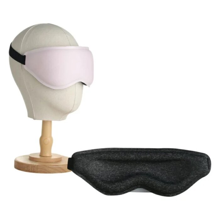 Två ögonmasker, en rosa på ett dockhuvud och en svart liggande framför, mot en vit bakgrund.