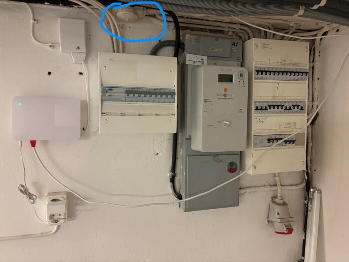 En fiberbox och elcentral på en vägg med olika elkomponenter och ledningar, med en markerad sektion i blått upptill.