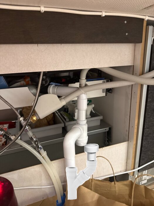 Vattenrör och avloppssystem under diskbänk med synliga plastkopplingar och slangar.