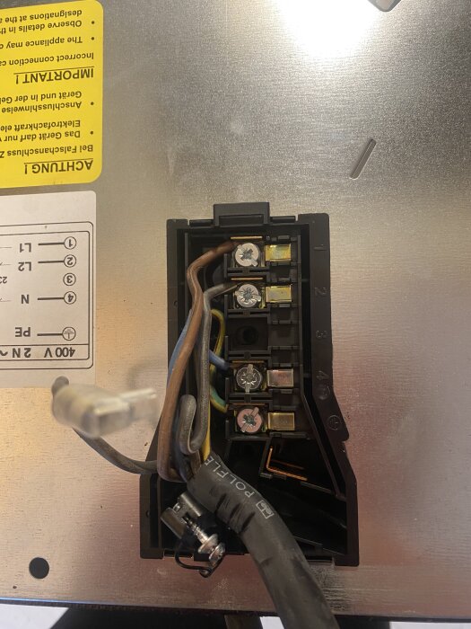 Närbild på en elektrisk kopplingsplint med fem anslutningspunkter och fyra kablar anslutna till en induktionshäll.