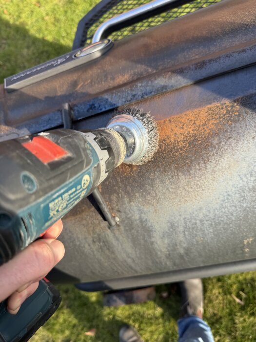 En person slipar bort rost med en stålborste på en borrmaskin från en offset smoker-grill.
