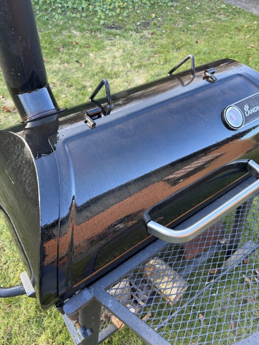 Bild av en nyligen inoljad offset smoker-grill med svart yta och metallhandtag, stående på en gräsmatta.