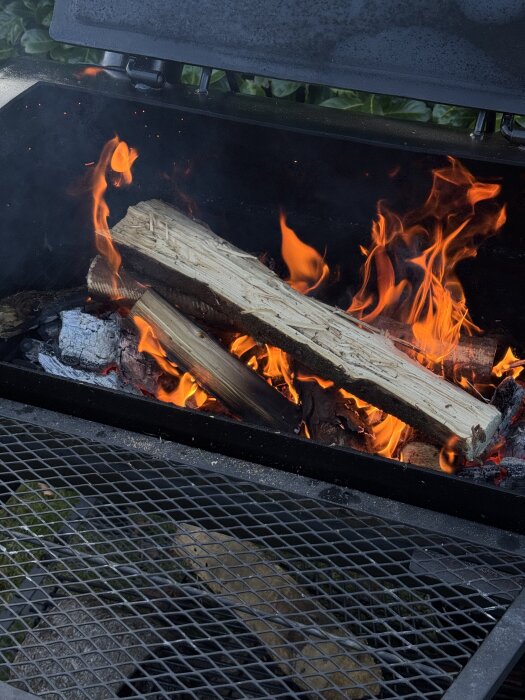 En tänd offset smoker-grill med lågor och ved.