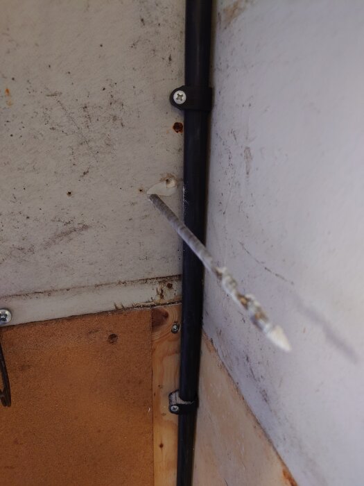 Borr rakt genom väggen bredvid svart kabel fäst med hållare, visar installation av laddbox och nätverkskabel i trångt utrymme.