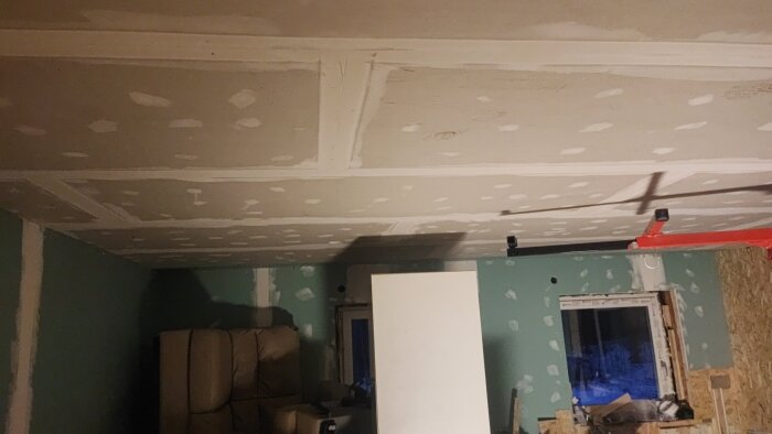 Tak med pågående renovering, oslipade spackelremsor och saknade skivor. Byggmaterial syns i rummet.