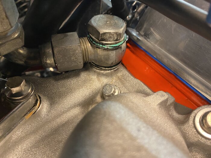Närbild av en metallkoppling på en kylarslang med synlig blågrön tätningsmassa, omgiven av motorblock och andra metalldelar.