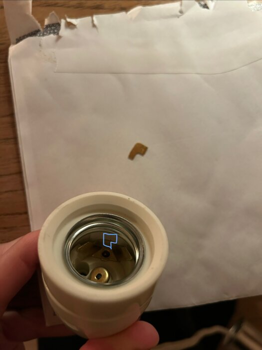En hand håller en lamphållare där ett bleck av metall syns vid sidan om, placerat på ett papper.