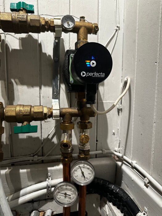 VVS-installation med Perfecta-pump, tryckmätare, ventiler och kopparrör i en vitmålad teknisk källare.