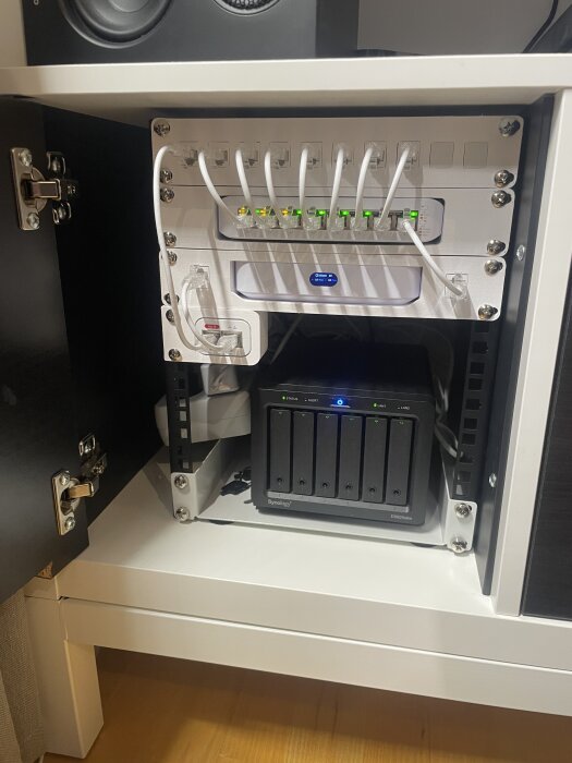 Teknikutrymme med nätverksswitch och NAS-enhet, installerade i en Ikea Kallax TV-bänk, med kablar och moduler arrangerade.