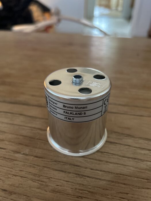 Metallcylinder på bord med etikett som visar designer Bruno Munari och modellnamnet Falkland S, tillverkad i Italien.