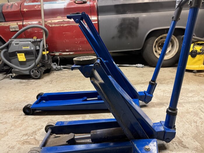 Blå garagedomkrafter i en verkstad med en röd bil i bakgrunden.