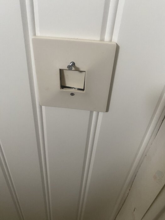 Vit vägg med väggpanel och infälld strömbrytare, där knappen ser ut att vara insänkt.