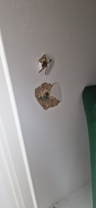 Vägg med två hål i en vit yta, där det övre hålet är mindre och det undre större med synligt material inuti.