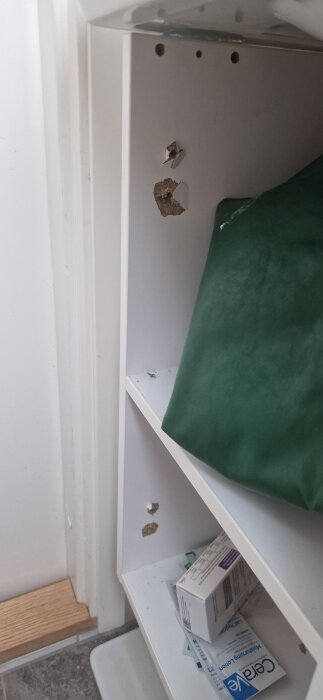 Bokhylla med hål i sidan, delvis fylld med förvaringslåda och medicinförpackningar.
