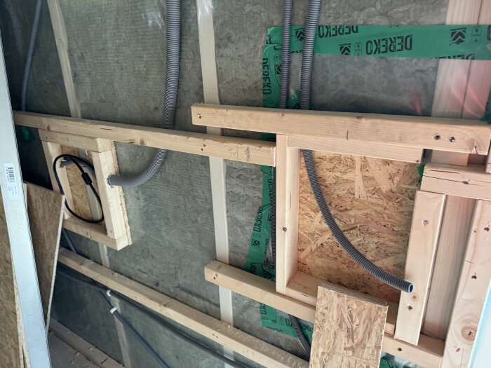 Träram och gröna rör i vägg med isolering. Synliga trästöd och byggmaterial i ett pågående bygg- eller renoveringsprojekt.