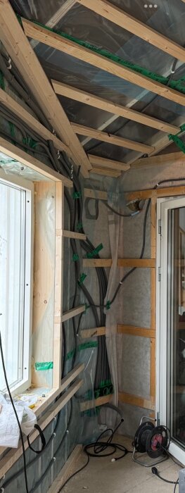 Renovering av rum med reglar, isolering och synliga elrör. Halvfärdigt tak och fönster syns, samt en elkabeltrumma på golvet.