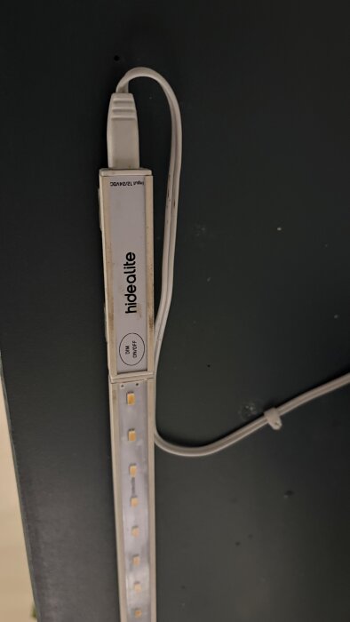 LED-list med texten "hidealite" och knappar märkt DIM och ON/OFF, monterad på en vägg. En kabel ansluts till en komponent.