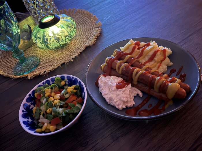Tallrik med korvar toppade med ketchup och senap, serverade med potatismos och sallad. Stämningsfull belysning från en grön dekorativ lampa.