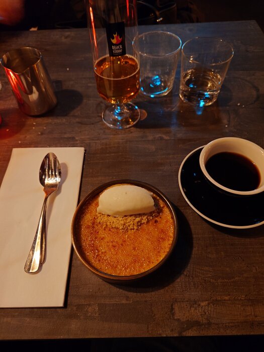 Créme brûlée med en kula äppelsorbet, placerad på ett bord med en kopp kaffe och en flaska dryck från Blackstone.