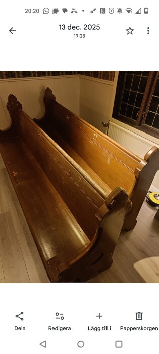 Gamla kyrkbänkar i mörkt trä med fläckar och avskavd färg, placerade inomhus på ett trägolv.