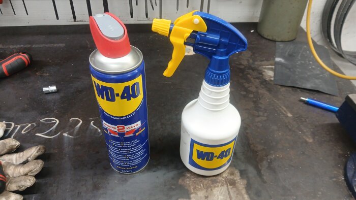 Sprayflaska och burk med universalspray, liknande WD-40, på arbetsbord; används för skydd av verktyg och maskiner mot rost.