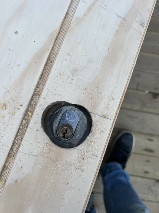 Närbild på en förrådsdörr med nyligen bytt plywood och ett borrat, överdimensionerat hål vid ett dörrlås.