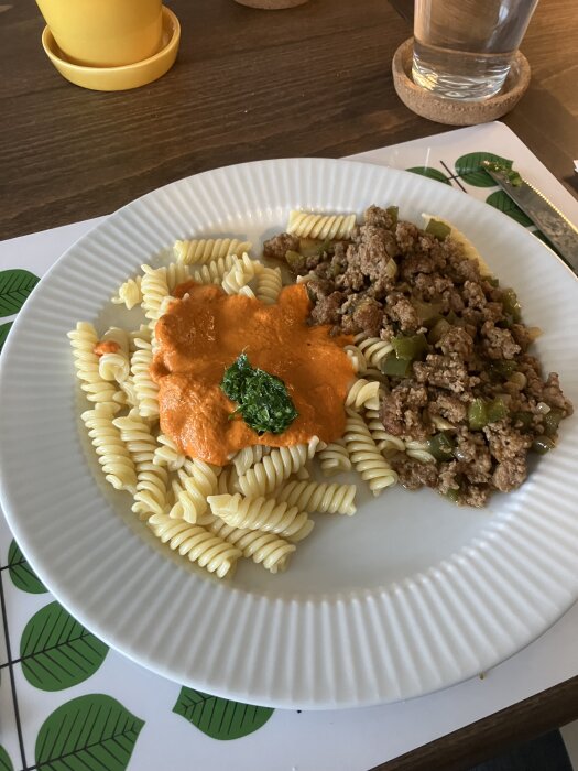 En tallrik med fusillipasta, röd sås och en grön örttopping, bredvid en blandning av köttfärs och grönsaker.