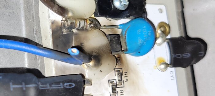 Defekta elektroniska komponenter på ett kretskort med blå och svarta kablar, potentiellt skadat efter överspänning.