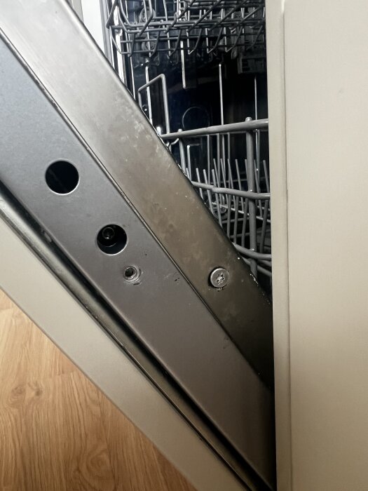 Öppen diskmaskin med synlig montering av luckan, skruv till vänster och insida av trådhyllor i ett kök.