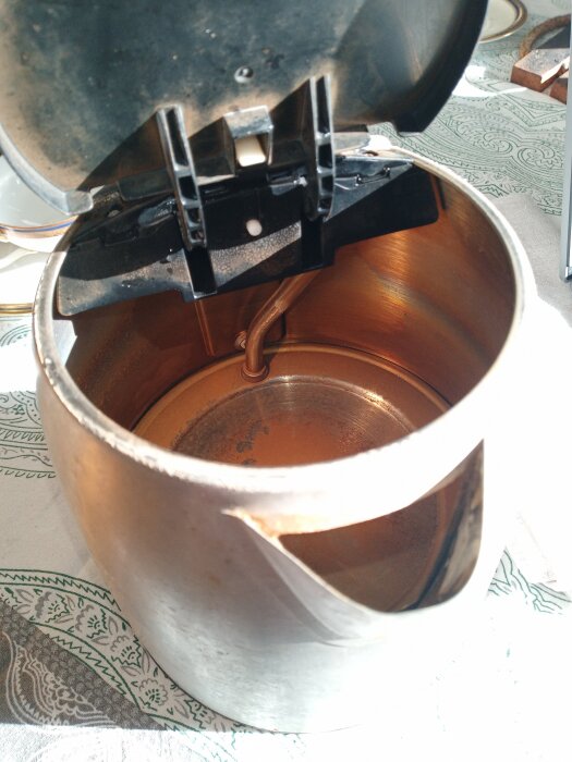 Öppen kaffebryggare visar insidan av kannan med lock uppfällt, exponerar metallytan och mekanismen.