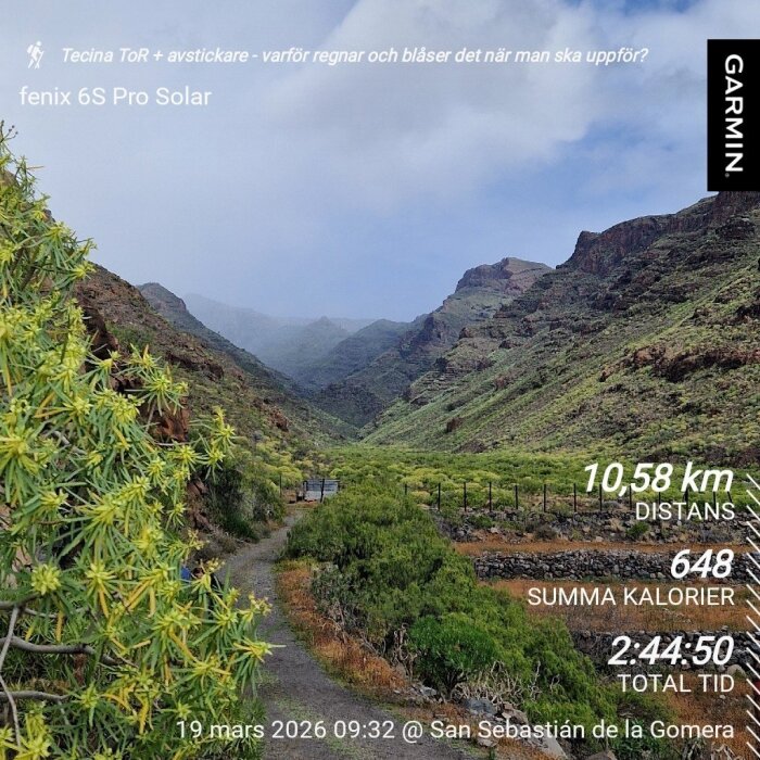 Vandringsled genom grönskande dal med berg i bakgrunden, molnigt väder. Garmin-data överlagrat: distans, kalorier och tid. San Sebastián de la Gomera.