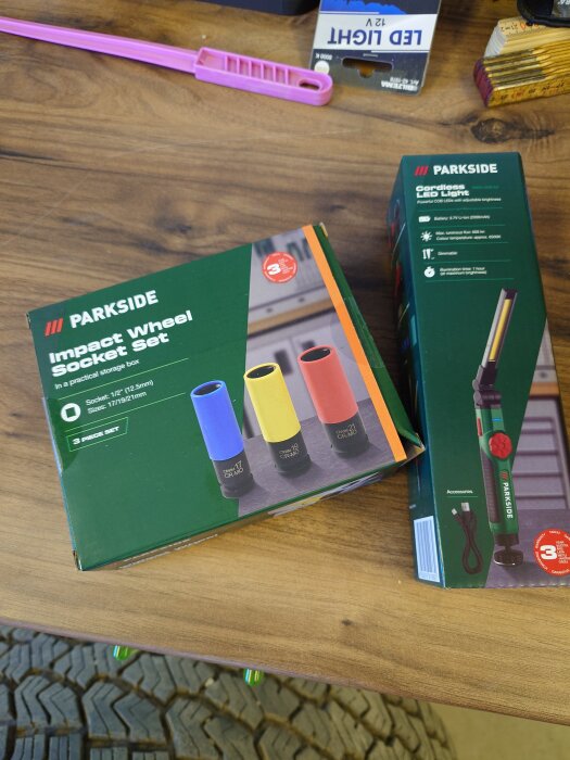 Två Parkside-produkter på ett bord: ett set med hjulmuttersocklar och en sladdlös LED-lampa i förpackningar.